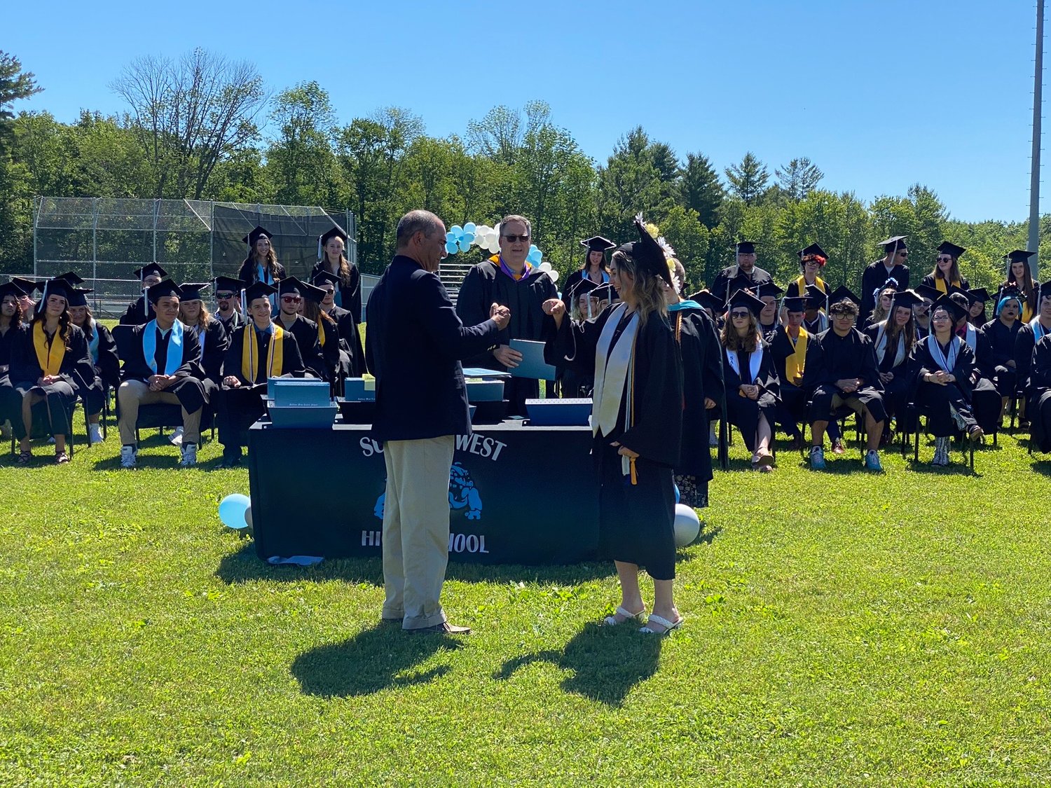 Ken Cohen, school board member, doing a special handshake with his daughter, Gabrielle Cohen, before presenting her diploma.